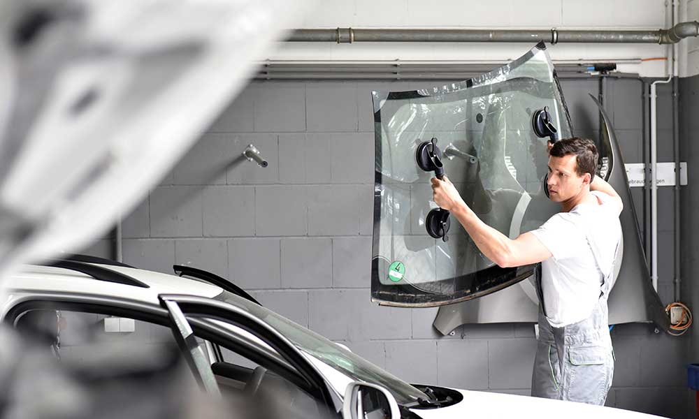 Mechaniker in einer Garage ersetzt defekte Windschutzscheibe eines Autos